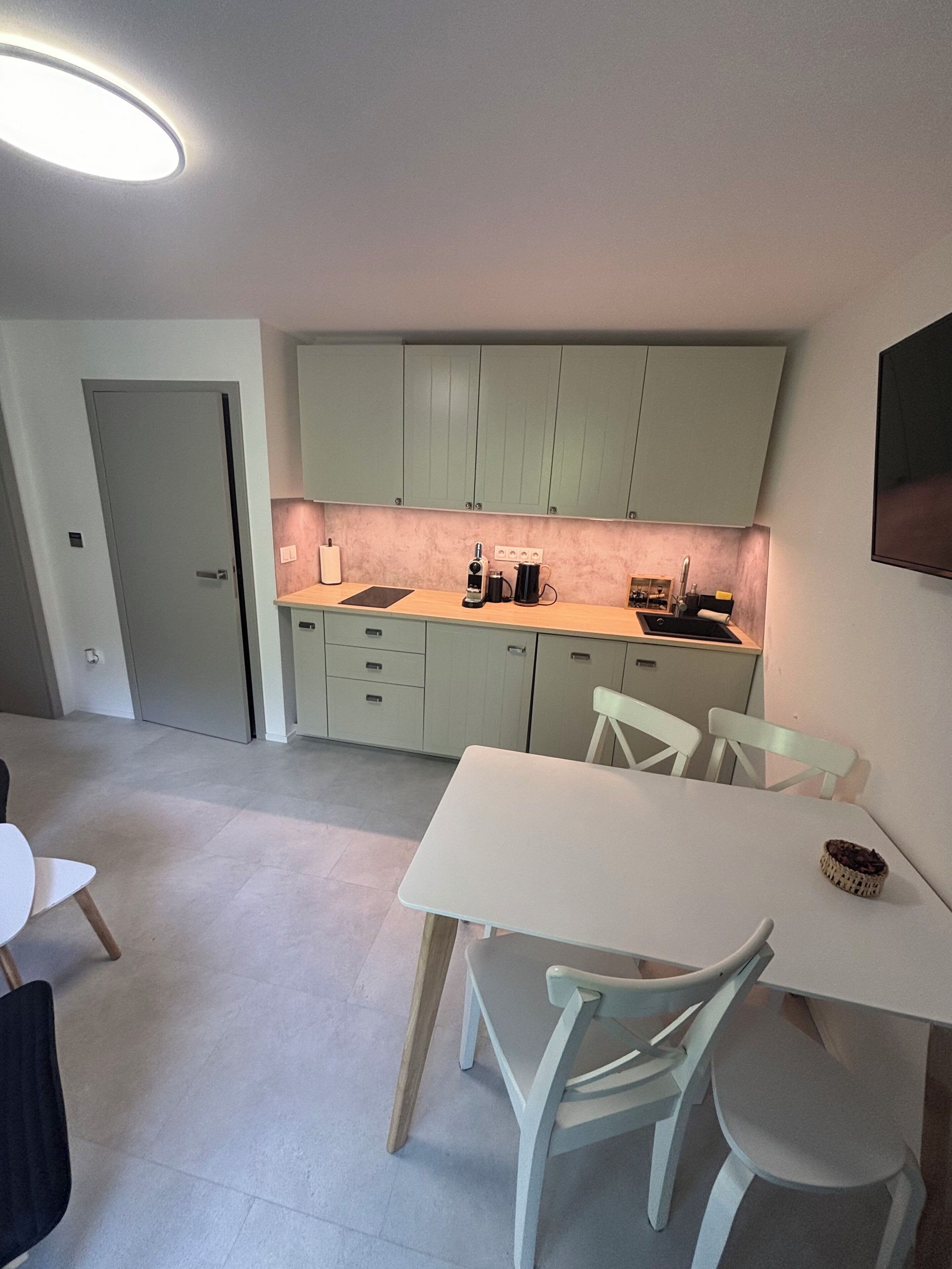 A modern kitchen with light green cabinets, a white countertop, and a dining area with a white table and chairs.