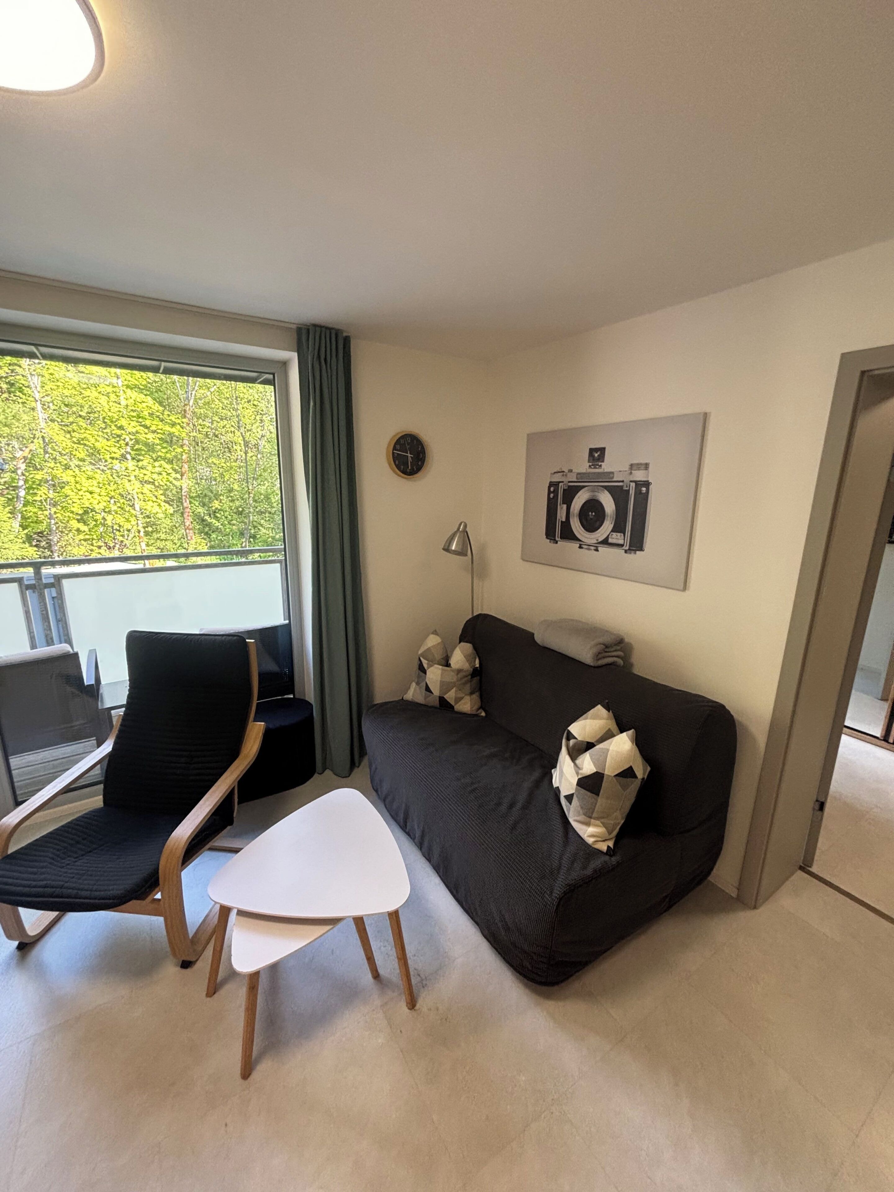 A modern living room with a sofa, a chair, a small table, a clock, and a camera on the wall.