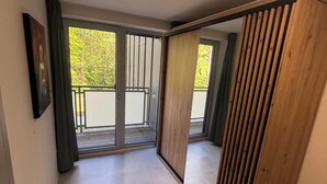 A room with a large sliding glass door leading to a balcony, a wooden partition wall, and a framed picture on the wall.