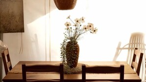 A wooden dining table with chairs, a hanging woven light fixture, and a vase with flowers.