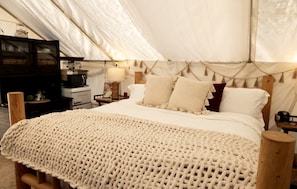 A tent with a bed, wooden furniture, and a kitchenette.
