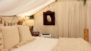 A tented room with a bed, a hanging plant, and a framed picture on the wall.