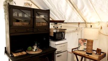 Une cuisine compacte équipée d’un four à micro-ondes, d’un petit réfrigérateur et d’une table en bois avec une lampe.