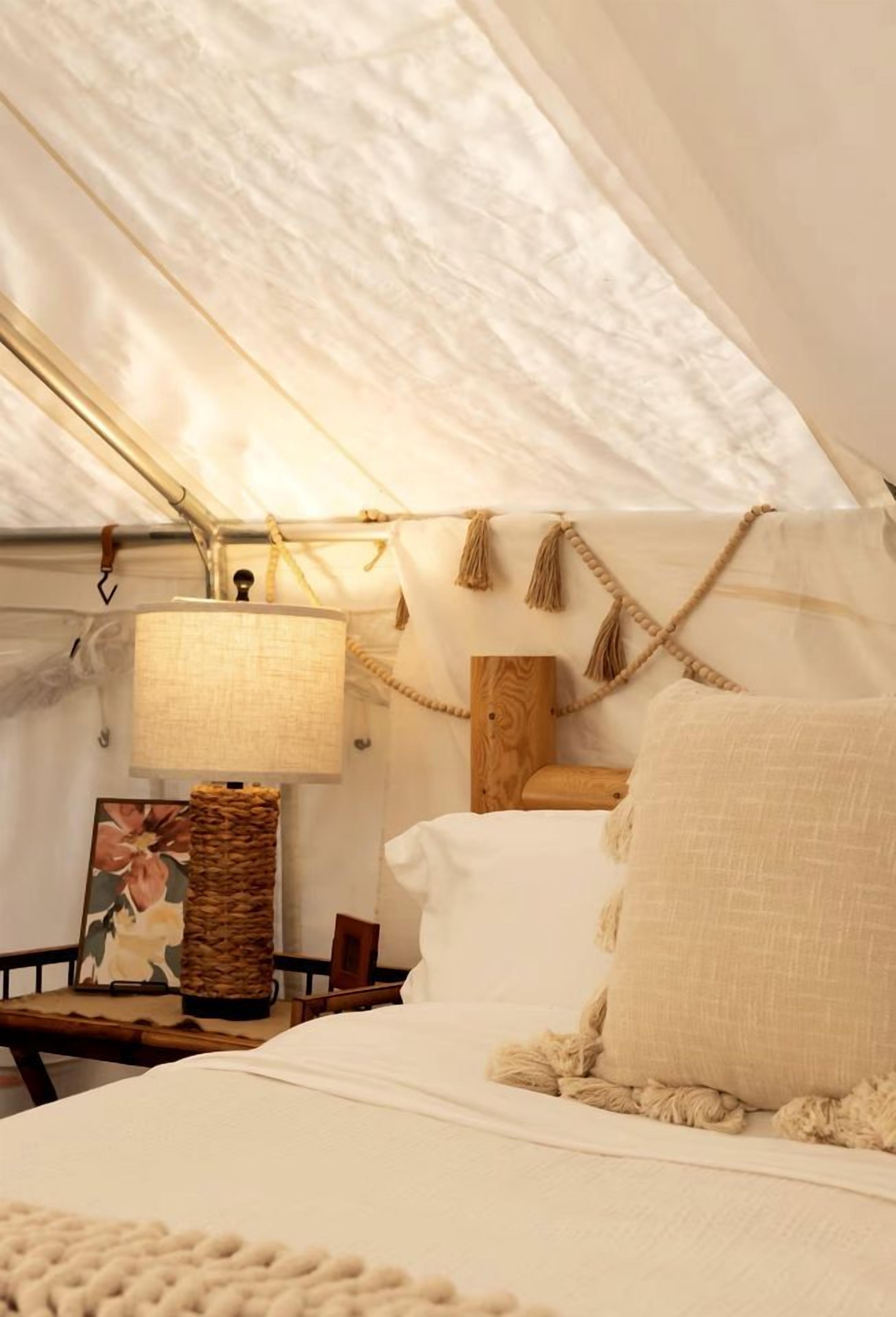 Une pièce aménagée comme une tente, avec un lit, une lampe suspendue, une tête de lit en bois et un panier tressé.