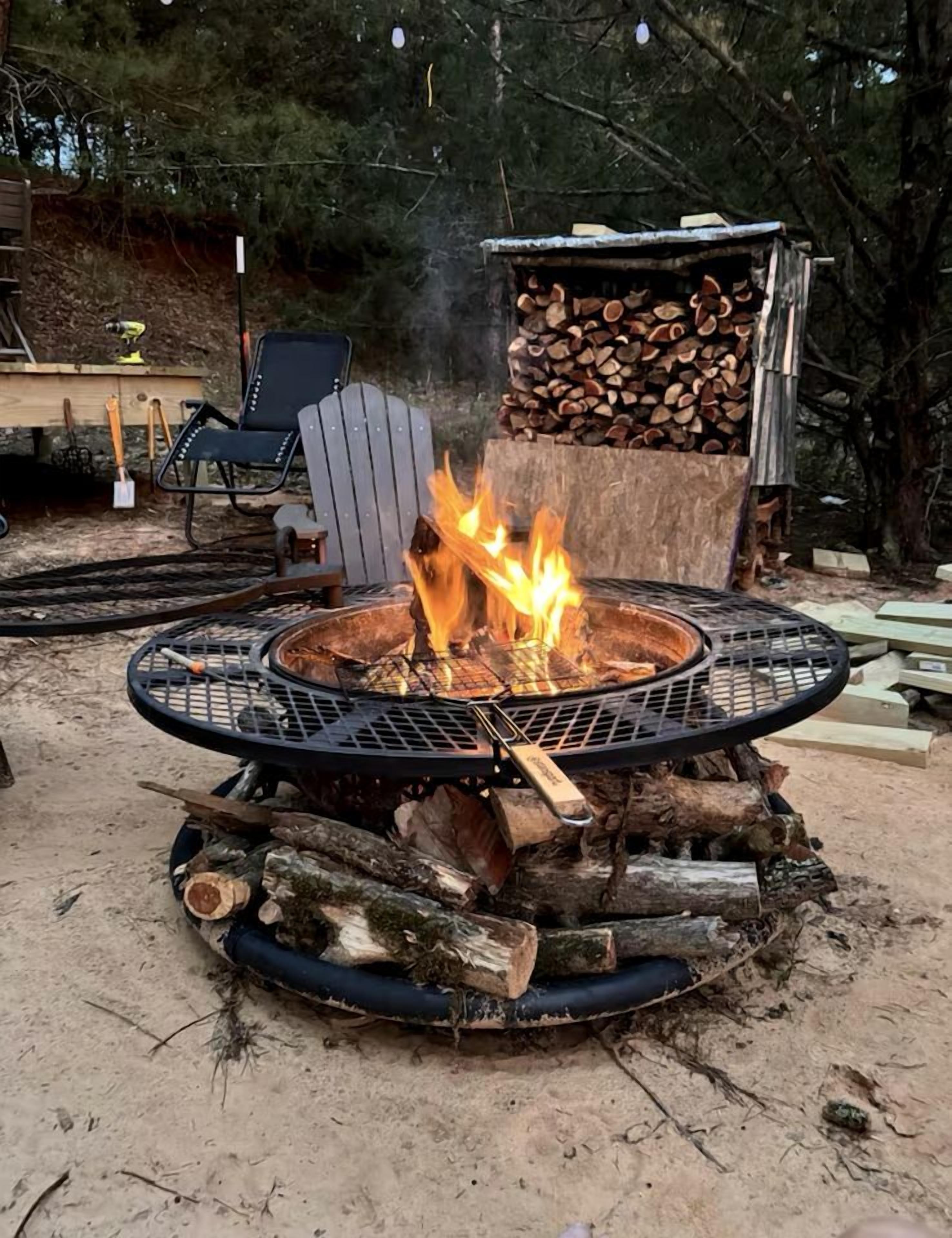Un hogar circular con llamas, rodeado de leña y una parrilla de metal.