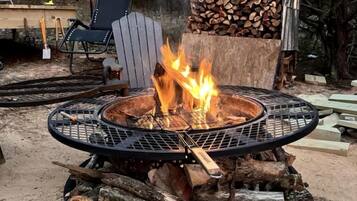 Un hogar circular con llamas, rodeado de leña y una parrilla de metal.