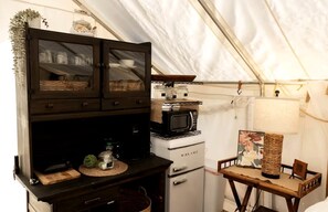 A compact kitchen with a microwave, a small refrigerator, and a wooden table with a lamp.