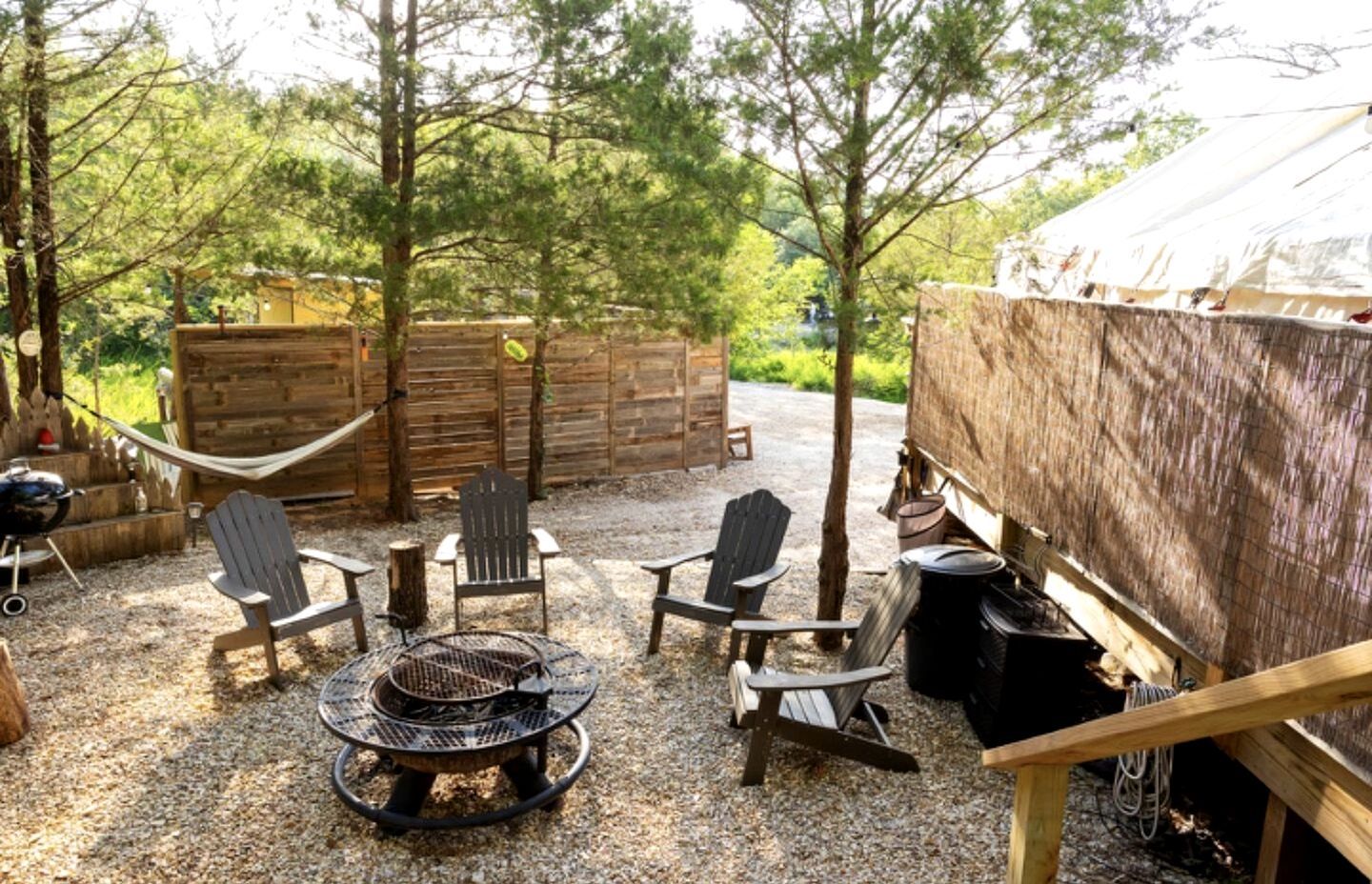 Un patio con mobiliario exterior, una fogata y una estructura de madera rústica.