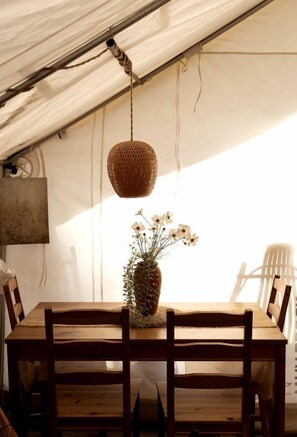 Una mesa de madera con sillas, una lámpara colgante tejida y un jarrón con flores.