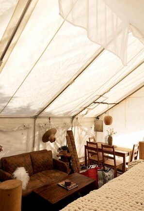 A tent interior with a sofa, wooden table, hanging basket, and a chair.