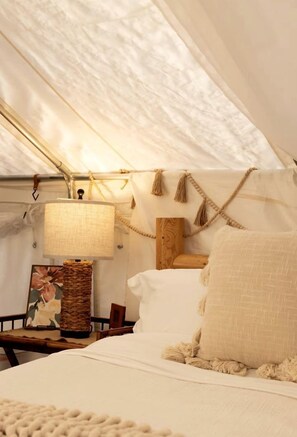 A tent-style room with a bed, a hanging lamp, a wooden headboard, and a woven basket.