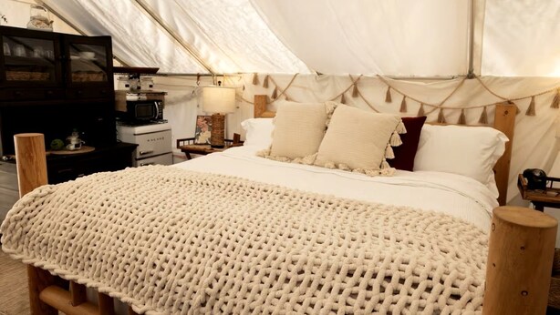 A tent with a bed, wooden furniture, and a kitchenette.