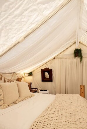 Una habitación con carpa, una cama, una planta colgante y un cuadro en la pared.