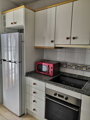 Eine Küche mit weißen Schränken, einem Edelstahl-Kühlschrank, einer roten Mikrowelle und einem eingebauten Backofen.