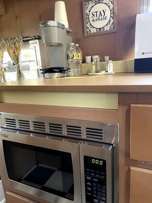 Eine Küche mit integriertem Mikrowellenherd, einer Kaffeemaschine und einem Schild mit dem Aufschrift 'Stay awhile'.