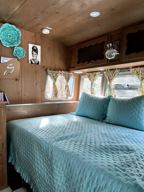 Ein gemütliches Zimmer mit einem Bett, Holzwänden, einem Fenster mit Vorhängen und einer Deckenleuchte.