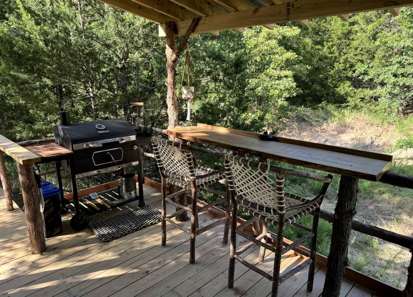 Une terrasse extérieure avec un barbecue, deux fauteuils en osier et une table en bois.