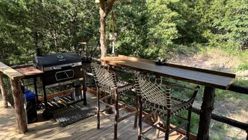 Une terrasse extérieure avec un barbecue, deux fauteuils en osier et une table en bois.
