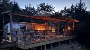 A rustic wooden deck with a covered seating area and a camper van. - Luxurious Remodeled Airstream with Wraparound Deck and Spa near Honey Grove, Texas (Honey Grove)