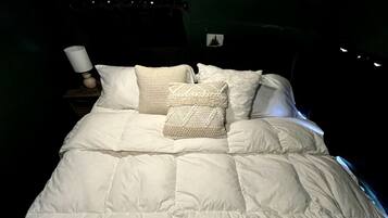 A bed with a white duvet and several pillows, a bedside lamp, and a small picture frame on the wall.