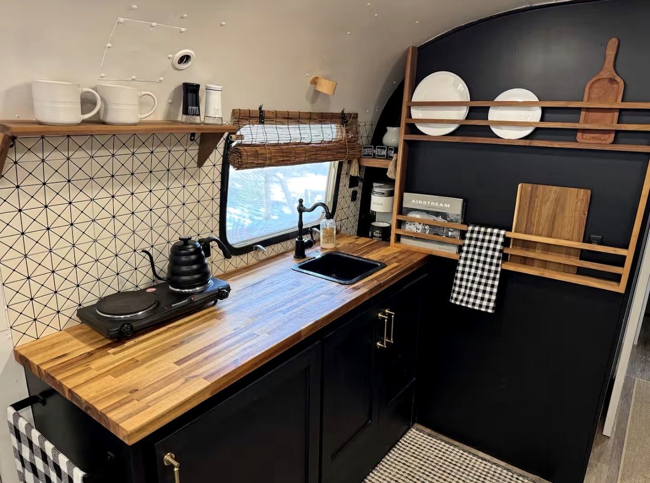 Une cuisine compacte dotée d’un plan de travail en bois, d’une bouilloire, d’une machine à café et d’un crédence noir.