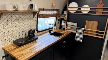 Une cuisine compacte dotée d’un plan de travail en bois, d’une bouilloire, d’une machine à café et d’un crédence noir.