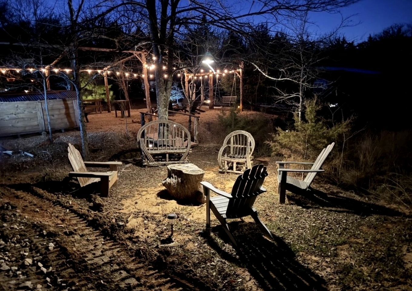 Un área de estar al aire libre con sillas Adirondack, una mesa de madera y luces colgantes.