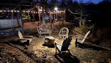Un área de estar al aire libre con sillas Adirondack, una mesa de madera y luces colgantes.