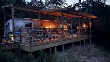 Une terrasse en bois rustique, dotée d’un espace salon couvert et d’un camping-car.
