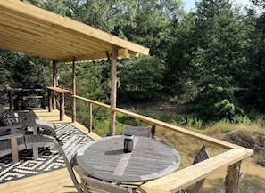 Eine Holzterrasse mit rundem Tisch und Stühlen, umgeben von einer naturnahen Waldlandschaft.