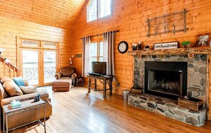 A log cabin interior with a stone fireplace, leather sofa, and a television. - Secluded Family Retreat in Log Cabin with Hammock and Fire Pit in Topton, North Carolina (Topton)