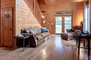 A log cabin interior with a wooden staircase, leather sofas, a desk with a computer, and a large window with a view. - Secluded Family Retreat in Log Cabin with Hammock and Fire Pit in Topton, North Carolina (Topton)