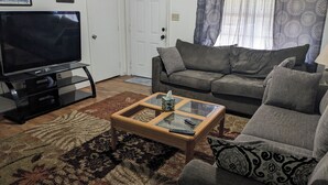Ein Wohnzimmer mit Fernseher, einer Couch, einem Couchtisch und einem gemusterten Teppich.