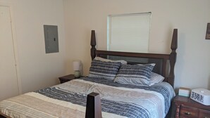 Ein Schlafzimmer mit einem Himmelbett, einem Nachttisch mit Lampe, einer Kommode und einem Fenster mit Jalousien.