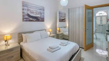 A hotel room with a bed, bedside lamps, a mirror, a wardrobe, and a door leading to a bathroom.