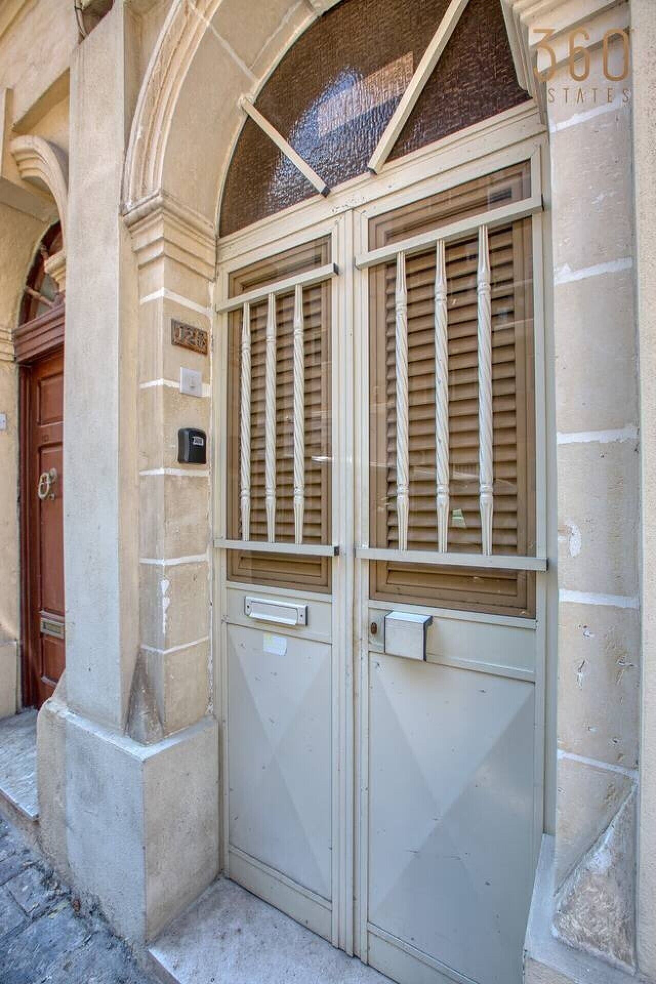 A double door with a metal grille, a small mailbox, and a number plate on the wall.