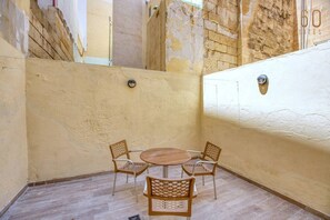 A small, enclosed patio area with a round table and four chairs, a tiled floor, and a textured wall. - Cosy 2BR Maisonette | 2BR Pietà | AC & Balcony (Tal-Pietà)