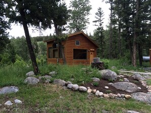 Une petite cabane en bois, entourée de rochers et d’arbres.