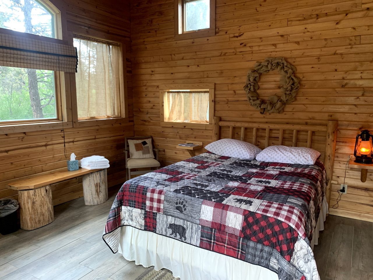 A wooden cabin bedroom with a bed, bench, and two windows.
