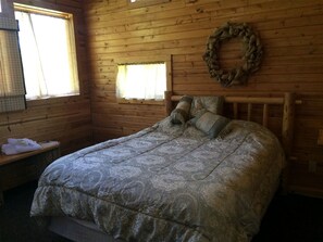 Une pièce de cabane en bois comprenant un lit, un banc, une fenêtre et une guirlande accrochée au mur.