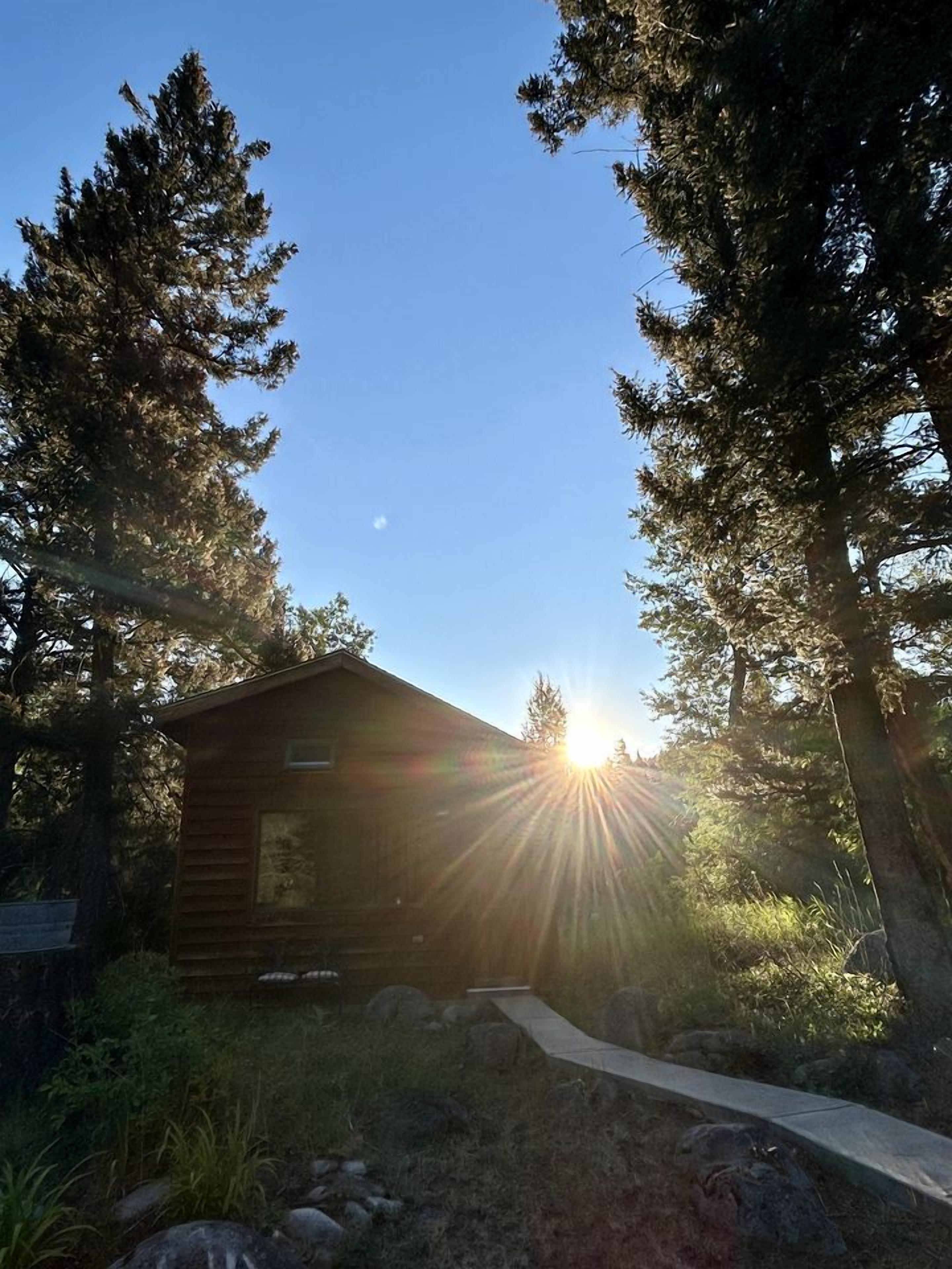 A small cabin with a clear view of the sun shining through the trees.
