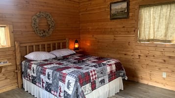 A wooden cabin bedroom with a bed, a wall-mounted lantern, a wreath, and a framed picture.