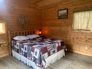 Un dormitorio de cabaña de madera con una cama, un farol en la pared, una corona y un cuadro enmarcado.
