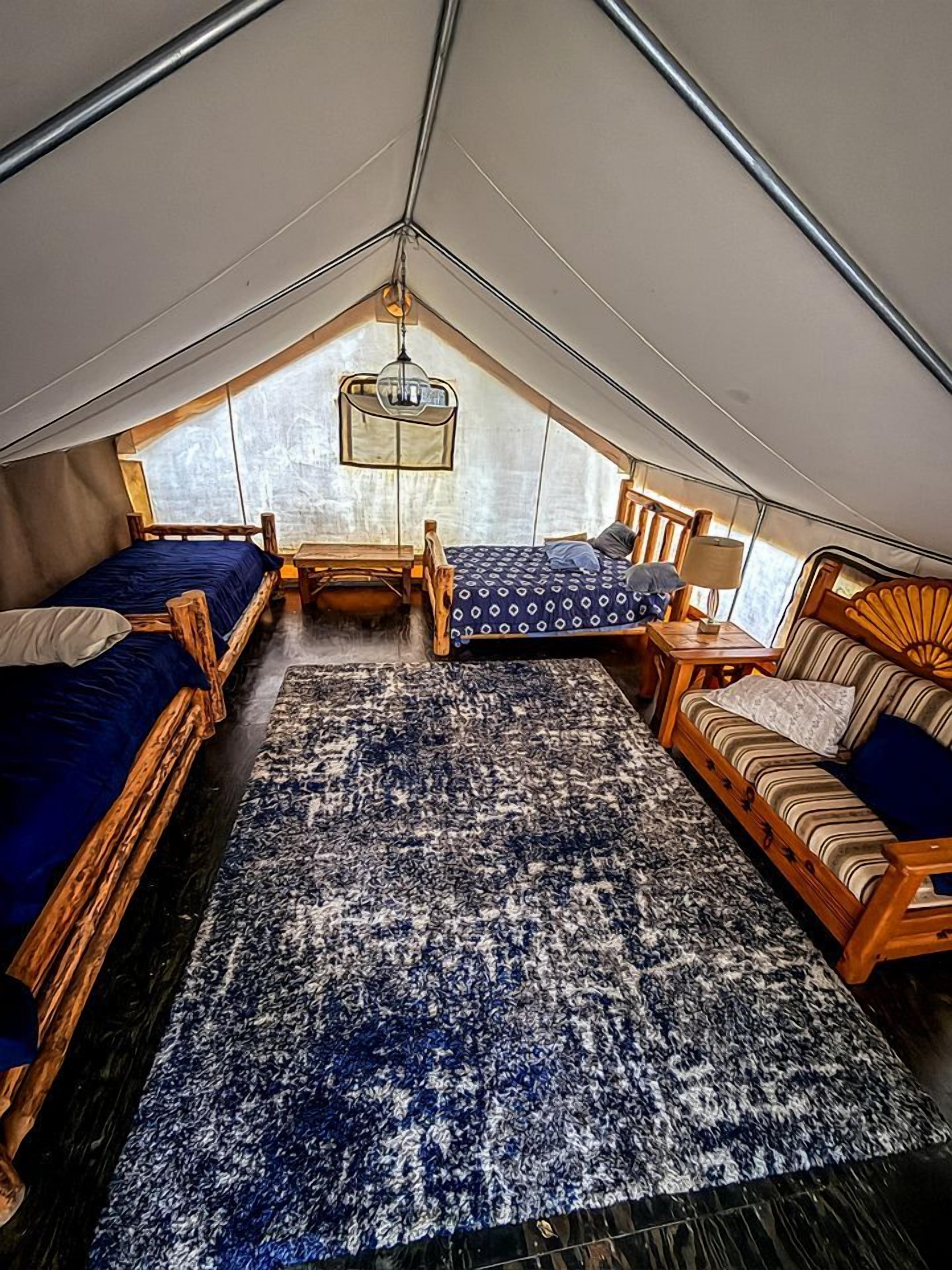 A tented room with two beds, a sofa, a rug, and a hanging light fixture.