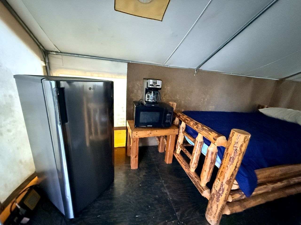 A compact room with a bed, a small wooden table, a microwave, and a refrigerator.