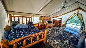 A tented room with a bed, a small table, a chair, and a view of the outdoors.