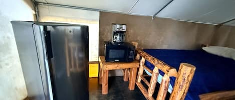 Una habitación compacta con cama, una pequeña mesa de madera, microondas y refrigerador.