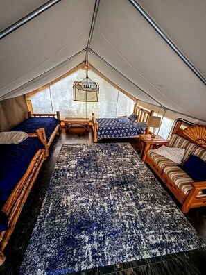 A tented room with two beds, a sofa, a rug, and a hanging light fixture.