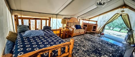 Um quarto com tenda, uma cama, uma mesa pequena, uma cadeira e vista para o exterior.