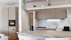 Eine moderne Küche mit Einbauofen, Marmor-Spritzschutz und einer Bar mit zwei weißen Stühlen.